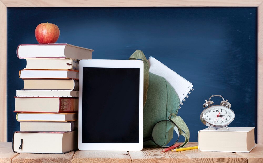 Tablet, stapel boeken en wekker voor schoolbord