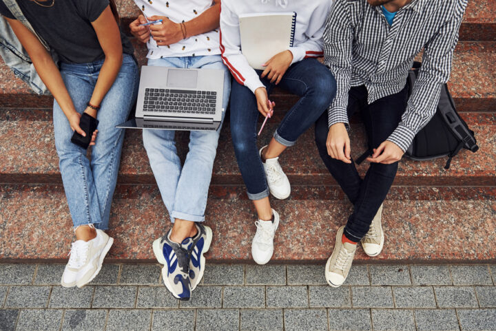 Scholieren zitten op een trap met een laptop en telefoon.