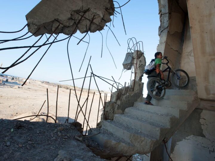 kind sleept fiets betonnen trap op in verder zwaar beschadigd gebouw op zandvlakte